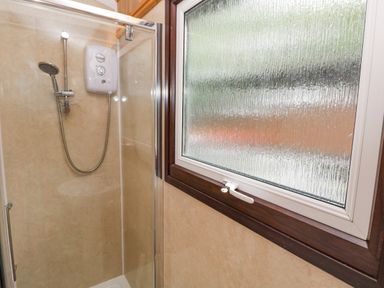 A shower with a glass door and a frosted window with a white handle at Doirewood Penlan Holiday Park near Cenarth