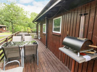 A wooden deck with outdoor furniture and a pizza oven on the wall at Doirewood Penlan Holiday Park near Cenarth
