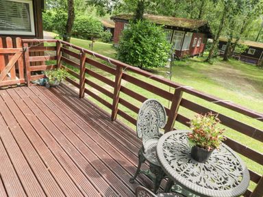 A wooden deck with metal table and chairs and a potted plant at Doirewood in Penlan Holiday Park near Cenarth