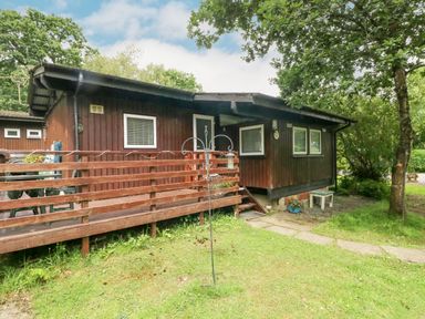 A wooden cabin with a deck and steps surrounded by grass and trees at Doirewood Penlan Holiday Park near Cenarth