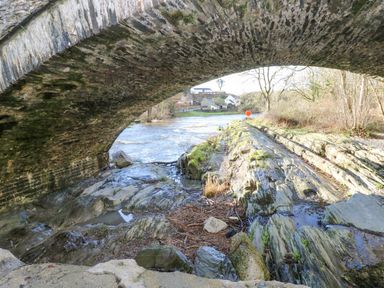 A stone arch bridge over a river with rocks and a grassy shore in a rural area at Doirewood in Penlan Holiday Park near Cenarth