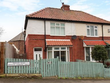 A two-story house with a red tiled roof and a green wooden fence with a private road sign at Over Esk in Whitby