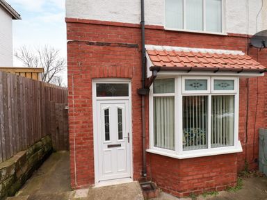 An exterior view of a brick house with a white door and bay window with vertical blinds at Over Esk in Whitby