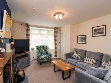A living room with a gray sofa, a floral armchair, a wooden coffee table, and a television at Over Esk in Whitby