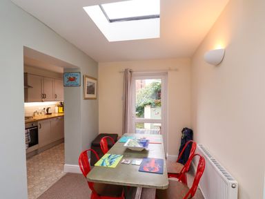 A dining room with a table and red chairs near a door and kitchen at Over Esk in Whitby