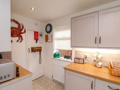 A kitchen corner with wooden countertops a microwave a wall clock a window with floral blind and a crab decoration on the wall at Over Esk in Whitby