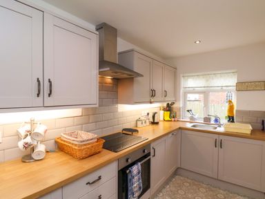 A kitchen with wooden countertops white cabinets a stove a sink and a window at Over Esk in Whitby
