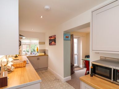 A kitchen with wooden countertops a microwave cups on a rack and a view into an adjoining room with a red chair at Over Esk in Whitby