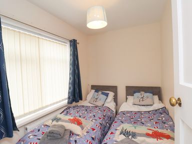 A bedroom with two single beds with nautical themed bedding and cushions at Over Esk in Whitby