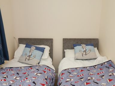 A bedroom with two single beds with anchor pillows and nautical themed blankets at Over Esk in Whitby