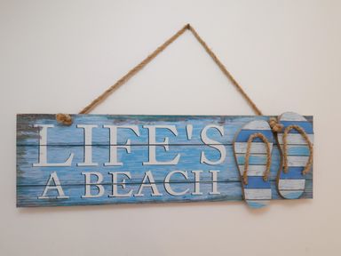 A wooden sign with the words Lifes a Beach and decorative flip flops hanging on a wall at Over Esk in Whitby