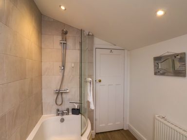 A bathroom with a bathtub and shower above it a towel on a glass shower screen a white door a fish shaped mirror on the wall and a radiator at Over Esk in Whitby