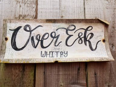 A wooden sign with the words Over Esk Whitby mounted on a wooden fence at Over Esk in Whitby