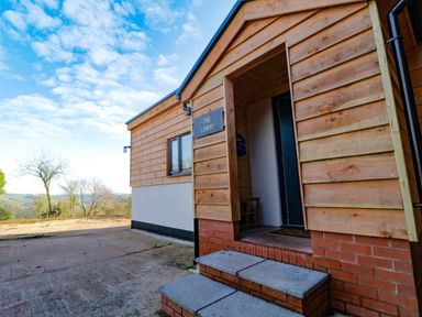 The entrance of a wooden house with steps leading to a door and a landscape in the background at The Linhay in Cadeleigh near Tiverton