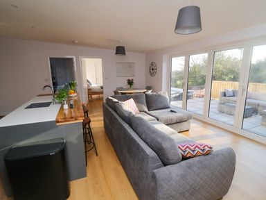 An open plan living room and kitchen with gray sofas wooden floor and large glass doors leading to a patio at The Linhay in Cadeleigh near Tiverton