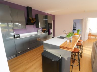 A kitchen with gray cabinets a wooden countertop bar with stools and an open door to a bedroom at The Linhay in Cadeleigh near Tiverton