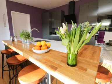A kitchen with a wooden island having stools fruit bowl and flowers at The Linhay in Cadeleigh near Tiverton