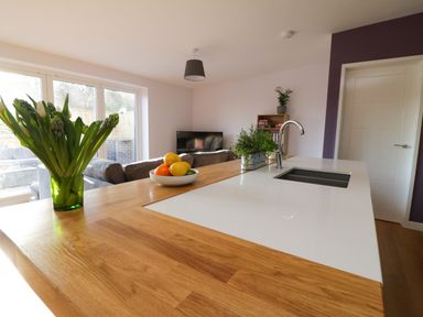 A kitchen countertop with a vase of flowers a bowl of fruit and a sink in an open living area at The Linhay in Cadeleigh near Tiverton