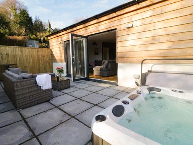 An outdoor patio with a hot tub sofa table with flowers and an open door to a living room at The Linhay in Cadeleigh near Tiverton