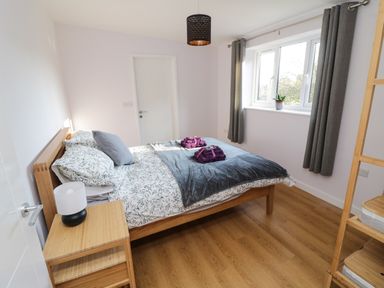 A bedroom with a wooden bed a nightstand a lamp folded towels on the bed and a window with curtains at The Linhay Cadeleigh near Tiverton
