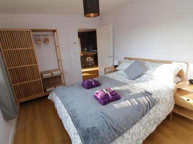 A bedroom with a double bed gray blanket purple towels wooden furniture and an open door to a kitchen at The Linhay Cadeleigh near Tiverton