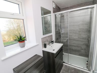 A bathroom with a shower enclosure sink cabinet mirror and a plant on the windowsill at The Linhay in Cadeleigh near Tiverton