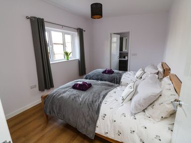 A bedroom with two single beds dressed with sheep patterned bedding and grey throws at The Linhay in Cadeleigh near Tiverton