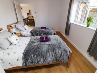 A bedroom with two single beds with gray blankets and purple towels on them at The Linhay in Cadeleigh near Tiverton