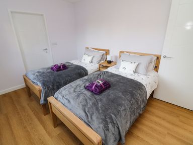 A bedroom with two single beds with gray blankets and purple towels on wooden floors at The Linhay in Cadeleigh near Tiverton