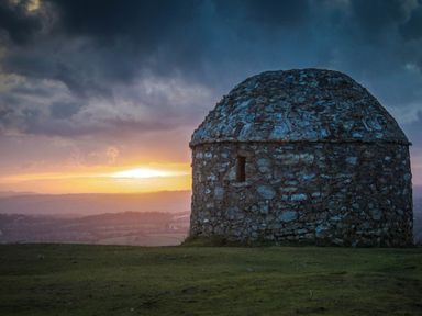 A stone roundhouse on a grassy hill at sunset with clouds in the sky at The Linhay in Cadeleigh near Tiverton