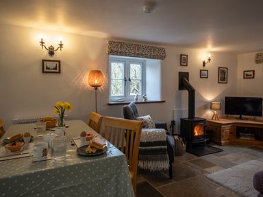 A dining table set for breakfast next to an armchair and wood-burning stove in a living room at Wavering in Compton Bishop near Axbridge