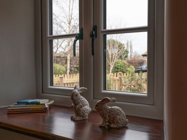 A windowsill with two rabbit figurines and a stack of books with a view of a garden and a wooden fence at Wavering in Compton Bishop near Axbridge