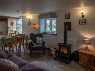 A living room with a wood burning stove an armchair a dining table and open wooden door at Wavering in Compton Bishop near Axbridge
