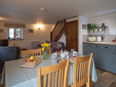 A dining table with breakfast items and a kitchen area with cabinets and appliances at Wavering in Compton Bishop near Axbridge