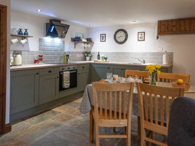 A kitchen with green cabinets a dining table with wooden chairs and yellow flowers at Wavering Compton Bishop near Axbridge