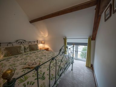 A bedroom with a metal bed frame and floral bedding a bedside table with a lamp and a window with curtains at Wavering Compton Bishop near Axbridge