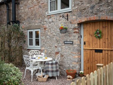 A stone house exterior with wooden door and small garden table with chairs at Wavering Compton Bishop near Axbridge