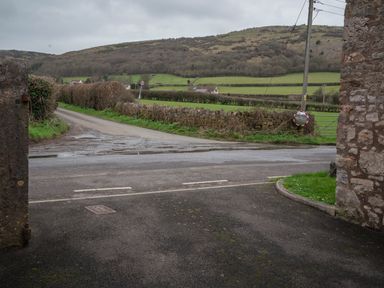 A countryside road with stone walls and hedges leading to fields and hills in the background at Wavering in Compton Bishop near Axbridge