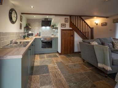 A kitchen with blue cabinets and a stone floor next to a gray sofa and wooden stairs at Crooks in Axbridge