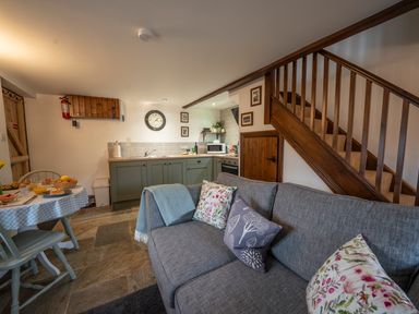 A small kitchen and dining area with green cabinets a gray sofa and wooden stairs at Crooks in Axbridge