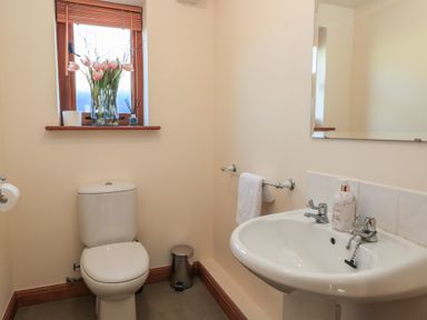 A bathroom with a toilet sink mirror window with flowers and a towel rail at Granary Cottage in Blackwell near Ilmington