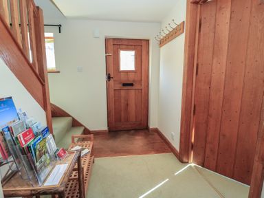 An entryway with a wooden front door a staircase a coat rack and a small table with brochures at Granary Cottage in Blackwell near Ilmington