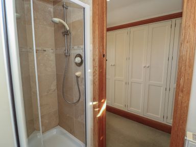 A shower with beige tiles and a sliding glass door next to a hallway with white built-in cupboards