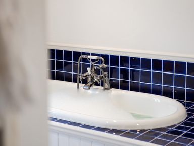 A bathtub with bubbles and a chrome faucet with dark blue tile backsplash at Victoria Lodge in Kingsbridge