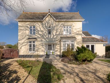 A large cream house with slate roof and gravel driveway with bushes and garden at Victoria Lodge in Kingsbridge