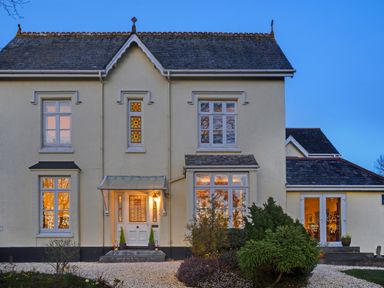The exterior of a two-story house with a front door with stained glass and several windows with reflections at Victoria Lodge in Kingsbridge