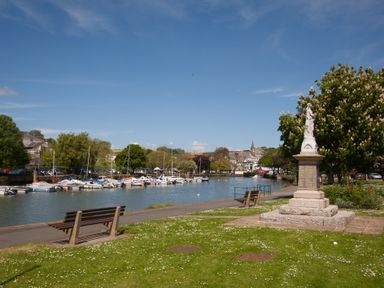 Benches along a river with boats moored and a statue near a tree at Victoria Lodge in Kingsbridge