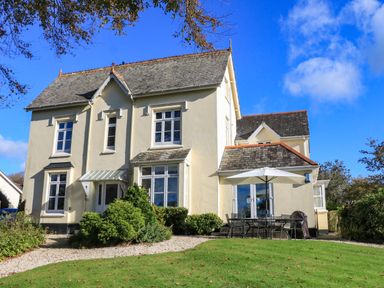 A cream colored two story house with a slate roof and garden furniture with umbrella on a lawn at Victoria Lodge in Kingsbridge