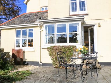 An outdoor patio with a small table and two chairs outside a cream house with large windows at Victoria Lodge in Kingsbridge