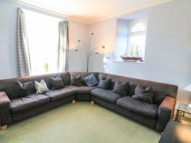 A living room with a large corner sofa and a model ship on the window ledge at Victoria Lodge in Kingsbridge
